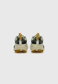 Sportieve schoenen met een bovenwerk van gaas in groen en zwart, met een gestructureerde beige zool en een gele lus aan de hiel.