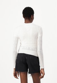 White knit sweater featuring a textured pattern and long sleeves, paired with black denim shorts that have frayed edges.