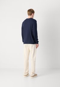 Marineblauwe longsleeve shirt met ronde hals, gecombineerd met lichte broek en beige schoenen, die een eenvoudige en ontspannen uitstraling laten zien.