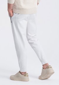 Witte sportieve joggers met tapered fit en zijzakken met rits, gecombineerd met beige sneakers met geperforeerde details en een textuur outsole.