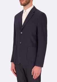 Blazer navy realizzato in tessuto testurizzato, con due tasche frontali, rever a punte e due bottoni, abbinato a una camicia bianca con colletto.
