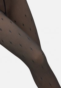 Pantys negras con un patrón que presentan una textura transparente adornada con pequeñas formas de diamante negras, brindando un diseño sutil pero distintivo.