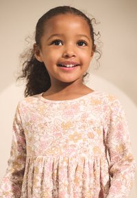 Klänning med lång ärm i mjukt, texturerat tyg med ljusrosa bakgrund och blommönster i gult och rosa. Veckad i midjan.