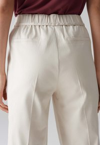 Lichtbeige broek met een gathers waistband, achterzakken en een gladde textuur; ontworpen met plooien voor een ontspannen pasvorm.