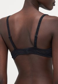 Reggiseno nero con spalline regolabili e un design arricciato. La parte posteriore presenta una chiusura a gancio e occhiello e una texture di tessuto liscia.