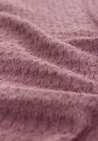 Tessuto mauve texturizzato con un motivo morbido e leggermente in rilievo, che mostra una superficie increspata con linee sottili in tutto.