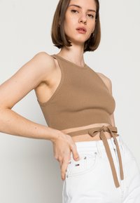 Top cropped castanho com textura, de design ajustado, apresentando uma cintura amarrada e um decote redondo, emparelhado com jeans brancos de cintura alta.
