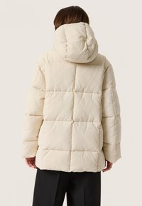 Gevoerde crèmekleurige jas met capuchon, met een doorgestikt ontwerp, oversized pasvorm en zijzakken. Gladde stof met een matte afwerking.
