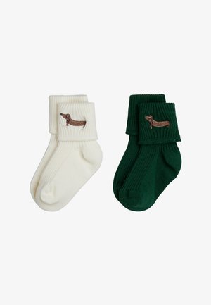 Par ribstrikkede ankelsokker i creme og mørkegrøn, hver med en broderet brun gravhund nær kanten.
