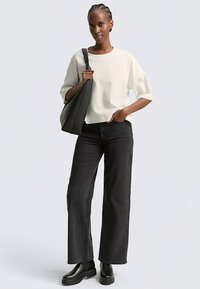 Weißer, locker sitzender Pullover, schwarze Jeans mit weitem Bein, schwarze Stiefeletten und eine graue Umhängetasche. Glatte Texturen und minimalistisches Design.
