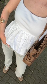 Top bianco senza maniche con tessuto arricciato in vita, abbinato a jeans grigi chiari e borsa in pelle marrone, indossato con sneakers grigie.