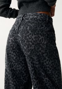 Pantalones de mezclilla con estampado de leopardo negro. Incluyen bolsillos traseros con solapas puntiagudas y una cintura ajustada. Textura sutil visible.