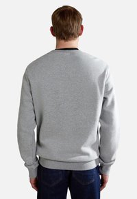 Felpa grigia con scollo a barca, polsini e orlo ribattuti. Il tessuto è morbido e strutturato. Indossata con jeans blu scuro.