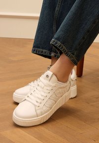 Witte sneakers met een gestructureerde leren bovenkant, voorzien van een patroonontwerp aan de zijkanten, platte veters en een dikke rubberen zool.