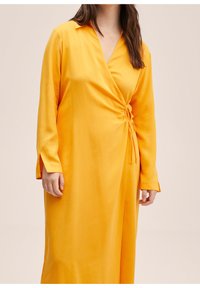 Gelbes Wickelkleid mit langen Ärmeln und Kragen. Mit gerafftem Detail in der Taille, das einen drapierten Effekt erzeugt. Glatte Stofftextur.