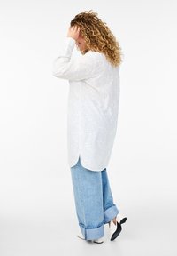 Weißes besticktes Langarmhemd mit floralem Muster, leicht abgerundetem Saum, kombiniert mit hellblauen weiten Jeans und zweifarbigen Absatzschuhen.