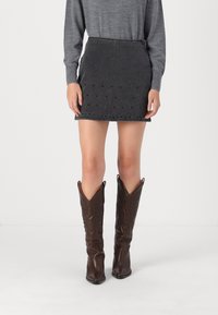 Denim mini krilo v temno sivi barvi s kovinskimi detajli ob robu, v kombinaciji s rjavimi usnjenimi kavbojskimi škornji, ki vsebujejo zapletene vzorce.