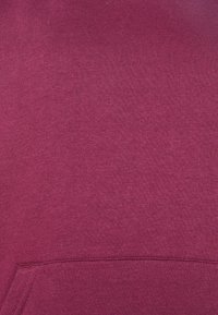 Sudadera con capucha burdeos con una superficie suave y texturizada, que presenta un bolsillo frontal y un diseño de pulóver sencillo sin patrones ni herrajes distintivos.