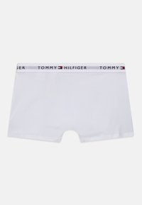 Baltie bokseri iz mīksta kokvilnas, ar pelēku jostasveidu, kurā ir rakstīts "TOMMY HILFIGER" un fona krāsas akcenti sarkanā un zilā krāsā.