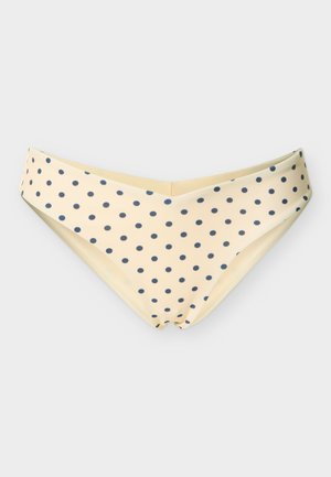 Krēmkrāsas bikini apakšdaļa ar platu V-veida jostasvietu un tumši ziliem punktiņiem, izlīdzināta uz balta fona.
