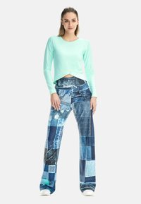 Mint green long-sleeve top with a twisted front design paired with denim-patterned wide-leg pants featuring various blue shades and textures.