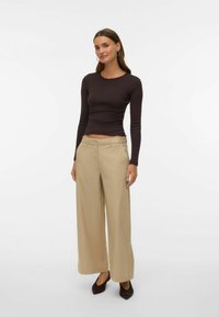 Melnas garām piedurknēm blūze un bēša krāsas plats kāju bikses, abas izgatavotas no gludas auduma. Biksēm ir pogas aizdare un sānu kabatas.