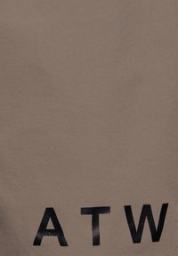 Taupe-tyg med en mjuk textur som har djärva svarta bokstäver "A T W" i botten. Designen är minimalistisk och modern.