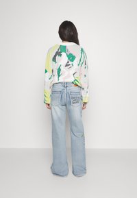 Suéter de punto colorido con patrones abstractos en verde, rosa y amarillo. Jeans de pierna ancha en azul desgastado con el texto "EL AMOR ES EL CAMINO PARA SER FELIZ" en la parte posterior.