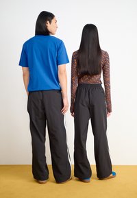 Blå crew-neck t-skjorte, svarte vide bukser med hvite sidestiper, og mønstrete langermet topp i varme toner. Glatt stofftekstur.