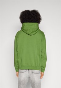 Green hoodie with a kangaroo pocket and drawstring hood, made of cotton blend fabric, paired with light gray jeans.