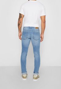 Slim-fit blå denimjeans med ljus tvätt, med bakfickor och en brun läderetikett på midjan. Bärs tillsammans med en vit t-shirt och sneakers.