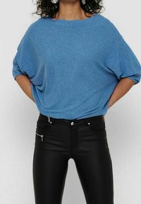 Haut en maille côtelée bleu avec un large col et une coupe ample, associé à un pantalon noir ajusté avec un détail de poche zippée.