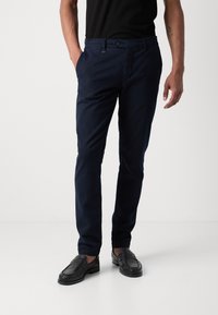 Chinos bleu marine avec une coupe slim, fabriqués en tissu doux. Comprend des poches avant, une fermeture à bouton et une texture lisse. Associés à des mocassins noirs.
