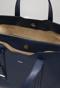 Granatowa skórzana torba na ramię o fakturowanym wykończeniu, z otwartym wnętrzem, brązowym podszewką oraz srebrnymi akcentami, w tym zamkiem błyskawicznym.