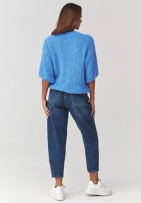 Puchaty niebieski sweter z krótkim rękawem, zestawiony z dopasowanymi ciemnoniebieskimi dżinsami i białymi sneakersami. Prosty design o teksturowanej powierzchni.