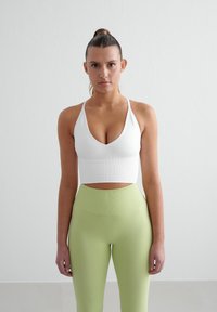 Top court côtelé blanc avec un décolleté en V et des fines bretelles, associé à un legging vert clair, lisse et taille haute. Design simple et ajusté.