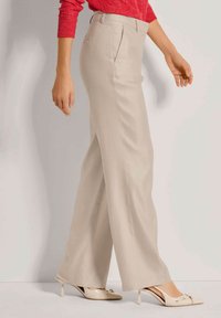 Beige wijde broek met plooien aan de voorkant en een lichte glans, gecombineerd met crèmekleurige hakken met een decoratieve accenten.