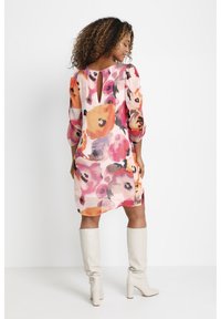Vestido floral y ligero en tonos de rosa, naranja y púrpura. Presenta mangas abullonadas y un escote de llave en la espalda, combinado con botas blancas hasta la rodilla.