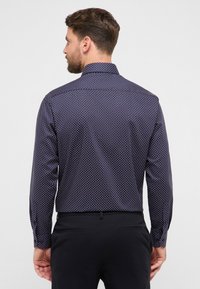 Camicia blu navy con bottoni e pois bianchi e rossi, caratterizzata da un colletto classico e maniche lunghe. Tessuto liscio con una vestibilità aderente.