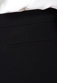 Svarta skräddarsydda byxor med en slät yta, åtsittande midja och ett enda bakfack med rektangulärt öppning. Minimalistisk design och rena linjer.