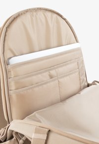 Bej színű hátizsák belseje párnázott laptopzsebbel, t�öbb tárolózsebbel és puha textúrájú béléssel rendelkezik.