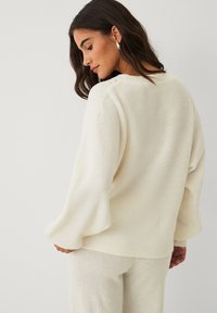 Elfenbeinfarbener Strickpullover mit einem lockeren Sitz, weiten Ärmeln und strukturierten Details an den Schultern. Weicher, leichter Stoff; schlichte Silhouette.