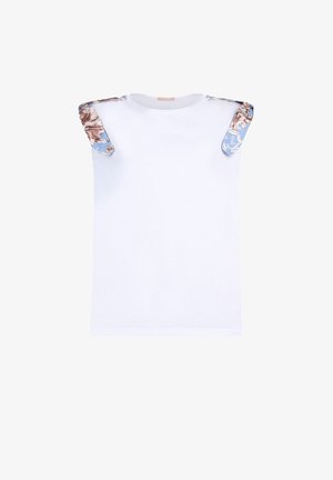White sleeveless shirt with shoulder details featuring blue fabric and brown floral patterns.