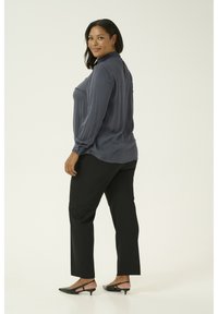 Blusa grigia a maniche lunghe con finitura testurizzata e polsini abbottonati, abbinata a pantaloni neri a gamba dritta e tacchi slingback neri.