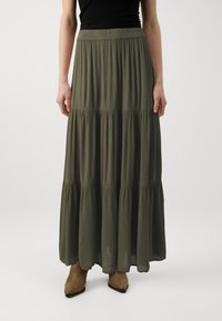 Jupe maxi verte olive avec un design à volants et un tissu doux et texturé. Présente une taille élastique et tombe doucement sous les chevilles.