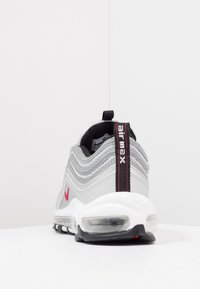 Tenisky Nike Air Max 97 v šedé barvě s vlnitým síťovinovým a syntetickým svrškem, červenými detaily, viditelným vzduchovým polstrováním a černou patní záložkou.