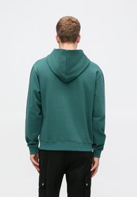 Hanorac verde cu glugă, realizat dintr-un material moale, cu o croială lejeră, mansete și tiv din tricot, având spatele simplu și fără detalii suplimentare.