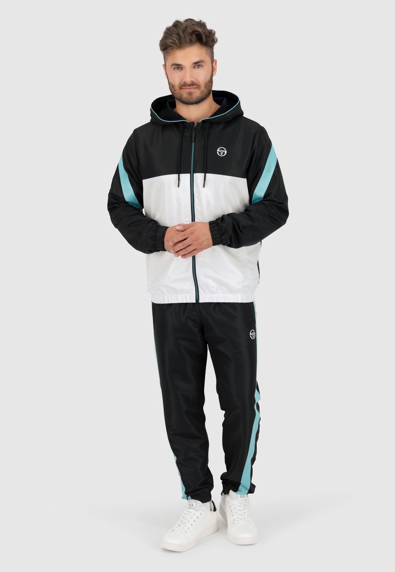 Zwart-wit trainingspak met turquoise accenten, met een ritssluiting capuchonjack en bijpassende broek. Gladde textuur, casual ontwerp.