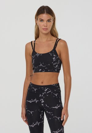 Top sportivo nero con un motivo marmorizzato, dotato di spalline sottili, design aderente e texture liscia. Abbinato a leggings coordinati.