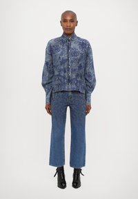 Blå denimskjorte med blomstermønster og knapper, kombinert med matchende jeans med teksturdesign. Brukt med svarte ankelstøvler.